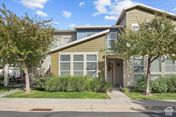 Multi-level exterior with mixed siding, multiple windows, established trees, and a concrete walkway