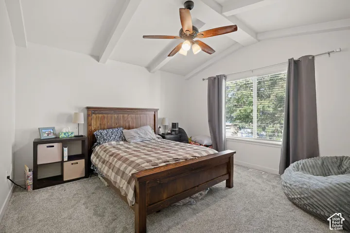 Vaulted ceiling with exposed beams, ceiling fan, carpeted flooring, and a large window