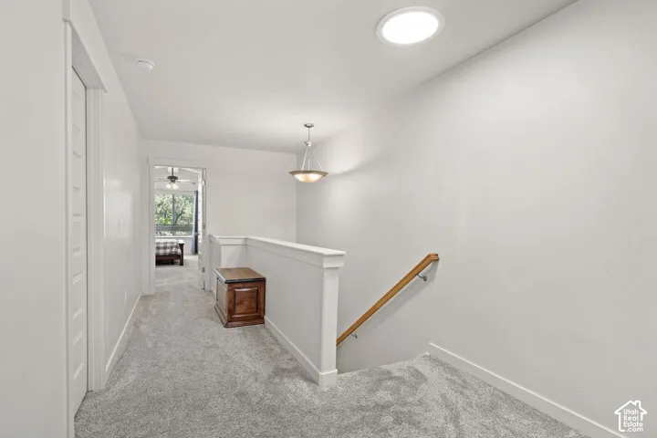 Carpeted hallway with white walls, white trim, and a white balustrade with a wood handrail
