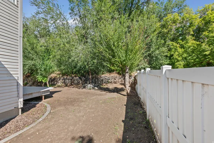 Private backyard featuring a white vinyl fence, mature trees, and a wooden deck