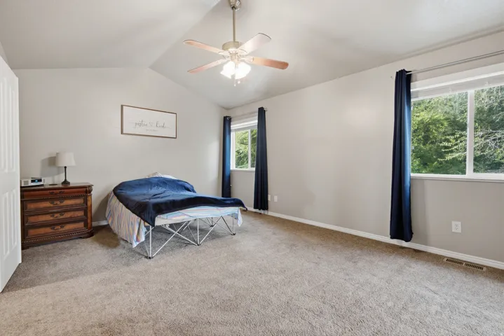 Vaulted ceiling with a ceiling fan, plush carpet flooring, and multiple windows