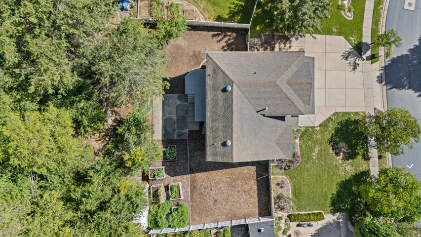 Pitched roof residence with an attached paved driveway, expansive mature trees, and a tiered garden area