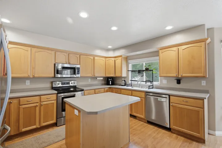 Kitchen featuring wood-finish flooring, light wood cabinetry, stainless steel appliances, a center island, and recessed lighting