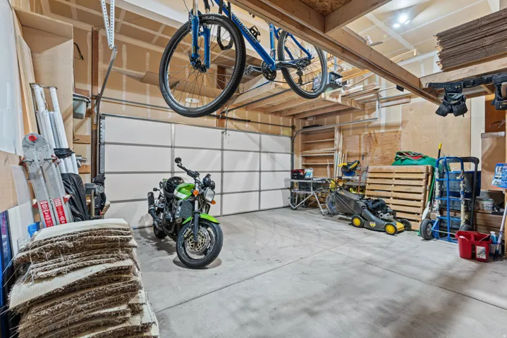 Concrete floor garage with a paneled overhead door, exposed wooden ceiling beams, and integrated lighting