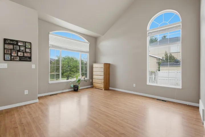 Vaulted ceiling, two arched windows, wood-finish flooring, neutral wall paint, and white trim
