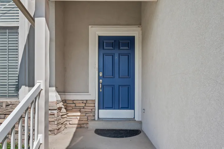 Entry with a paneled blue door, stone veneer accent, and stucco exterior