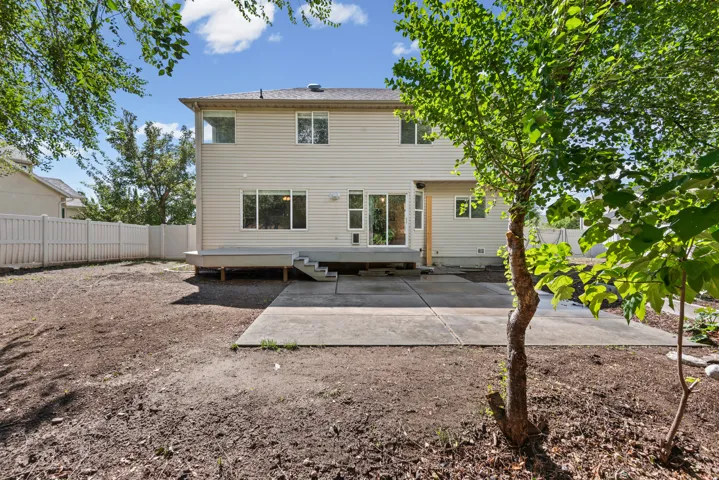 Expansive backyard with a full privacy fence, concrete patio, and a raised wood-finish deck with steps