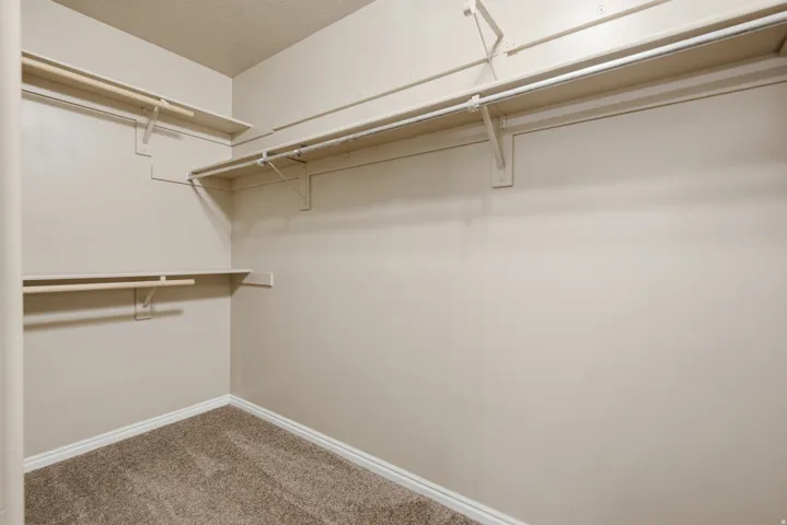 Walk-in closet featuring multiple shelving units, hanging rods, and carpet flooring
