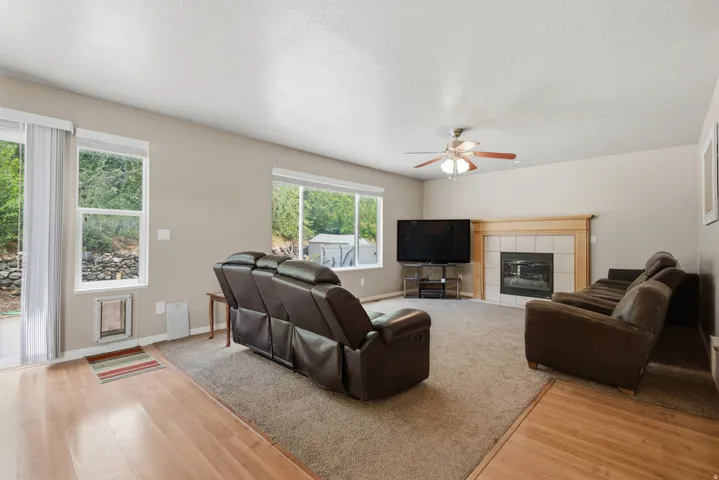 Living space featuring a fireplace with tile surround and wood mantel, ceiling fan, and wood-finish flooring