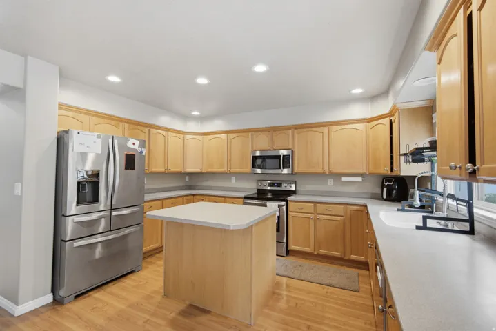 Kitchen featuring light wood-finish cabinetry, stainless steel appliances, a center island, and recessed lighting