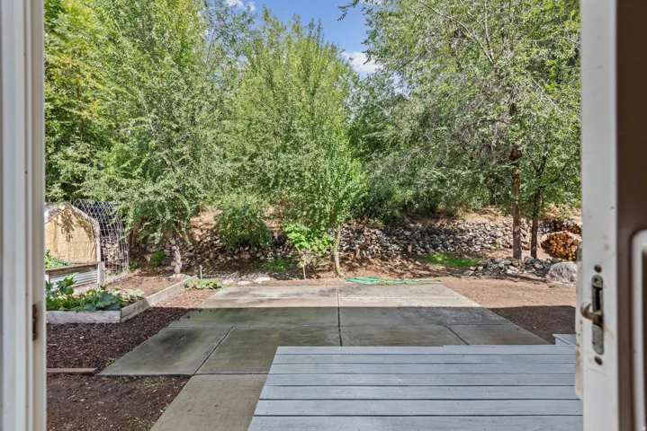 Outdoor patio with concrete and wood-finish decking, surrounded by mature trees and raised garden beds