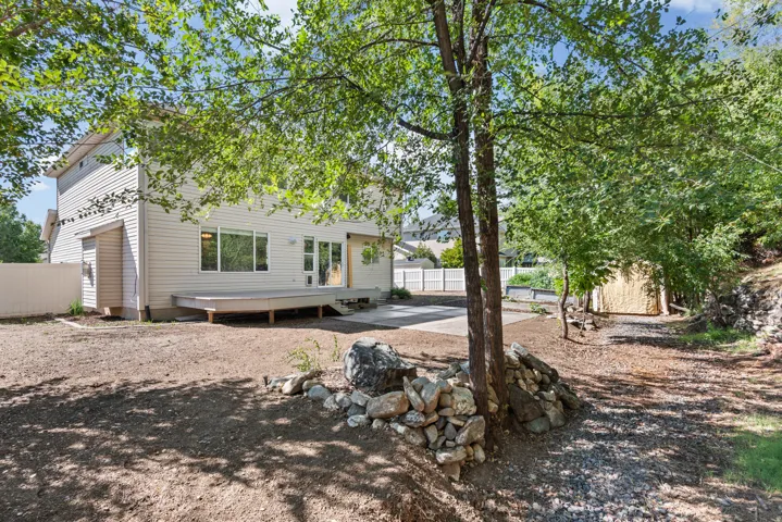 Rear exterior featuring light-toned siding, a spacious wooden deck, and a paved patio area