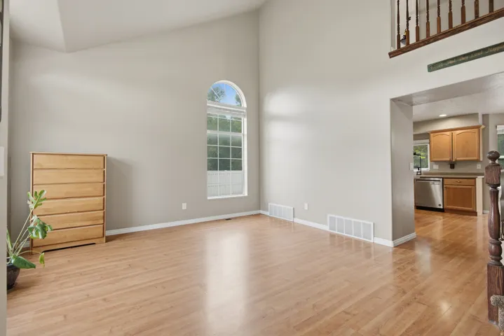Vaulted ceilings, arched window, wood-finish flooring, staircase with wood banister, and kitchen with wood cabinetry