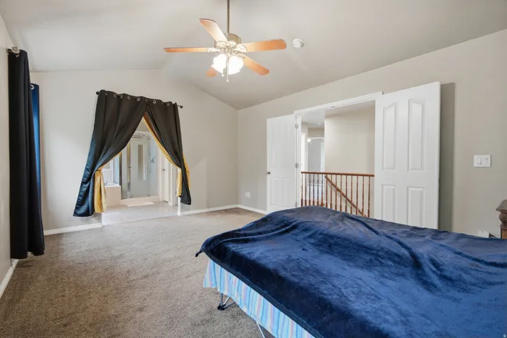 Vaulted ceiling with a ceiling fan, carpeted flooring, and double doors opening to a hallway