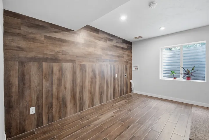 Wood-finish flooring, accent wall with wood paneling, recessed lighting, and a white-framed window