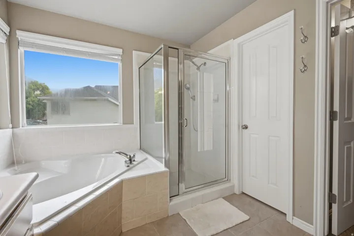 Corner soaking tub with tile surround, glass-enclosed shower, and tile flooring