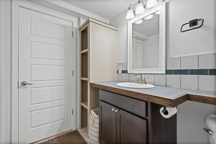 Single vanity with wood-finish countertop, undermount sink, and tiled backsplash