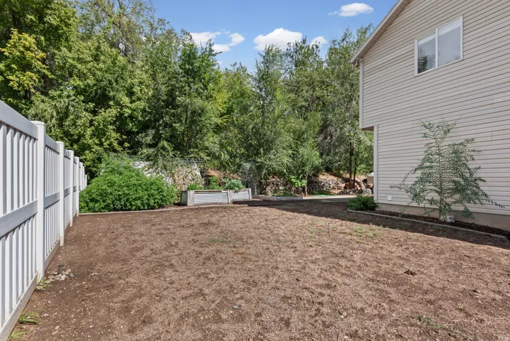 Spacious backyard featuring a white privacy fence, mature trees, and raised garden beds