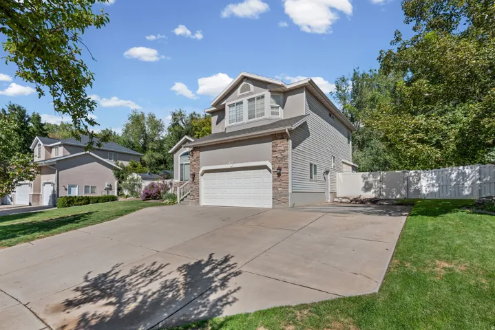 Stucco exterior with stone accent, concrete driveway, attached garage, and a fenced yard