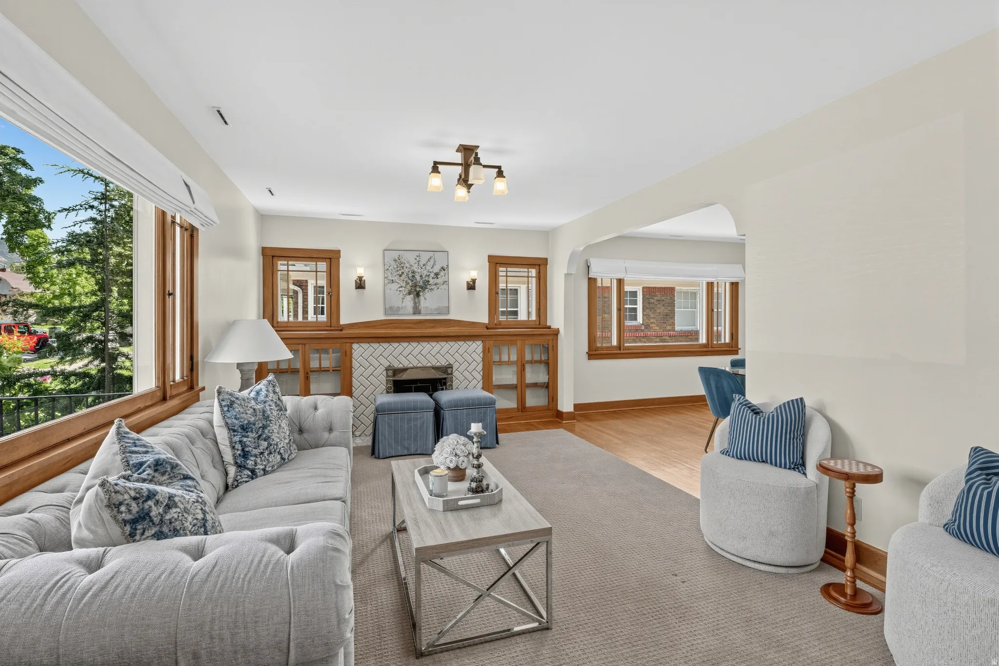Built-in cabinetry with glass panels, herringbone tile fireplace surround, wood window frames, wood-finish flooring, and a ceiling-mounted light fixture