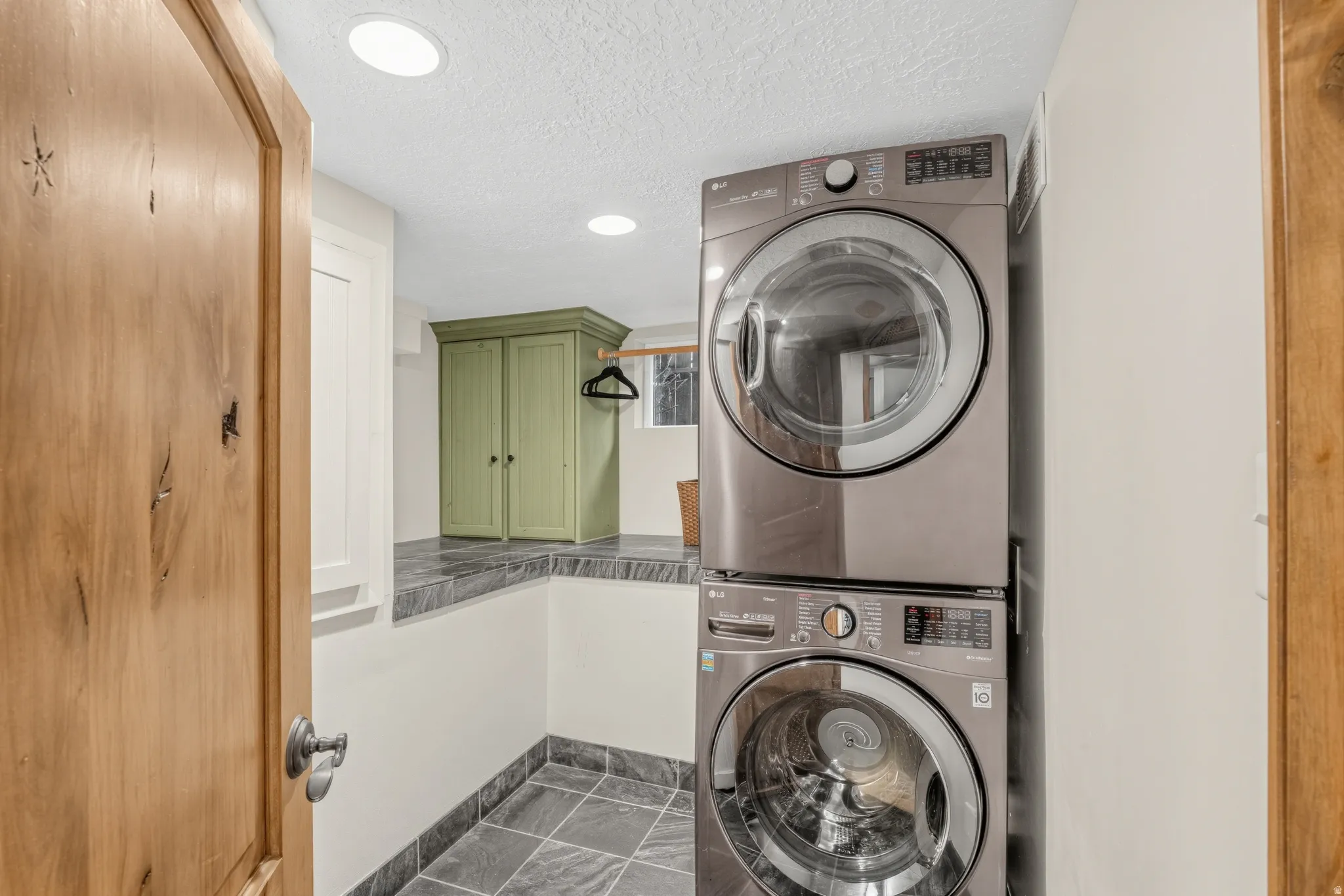 Laundry area featuring stacked appliances, stone-finish flooring, a stone-finish counter, and built-in cabinetry