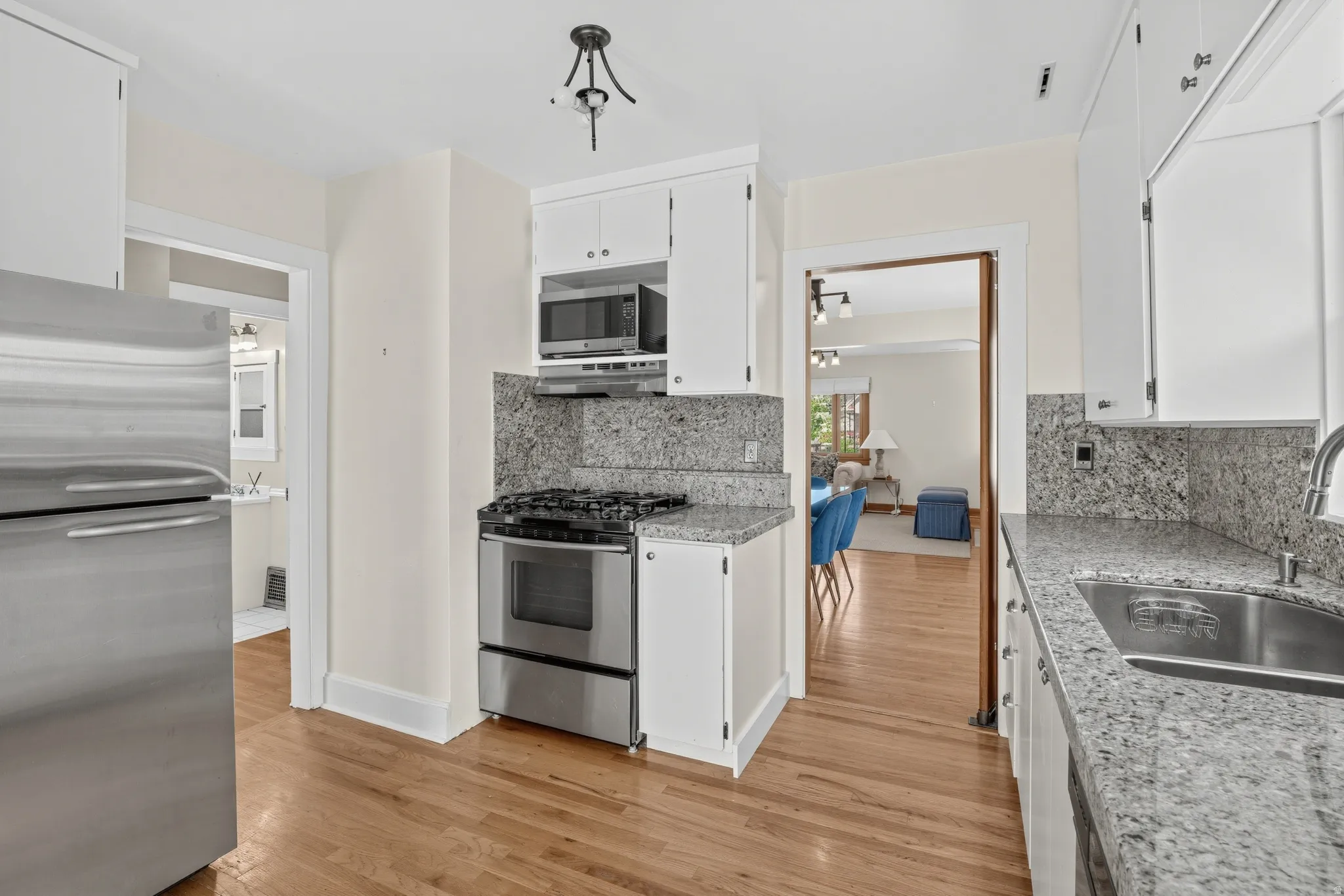 Kitchen with light wood-finish flooring, white cabinetry, integrated stainless-steel appliances, and granite countertops