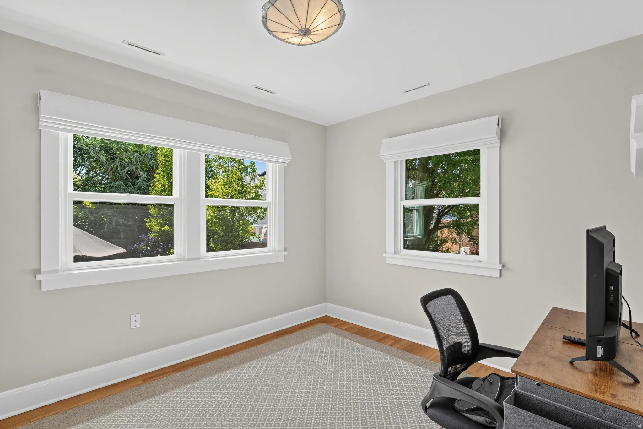 Bright room featuring two large windows, wood-finish flooring, and a semi-flush mount ceiling light