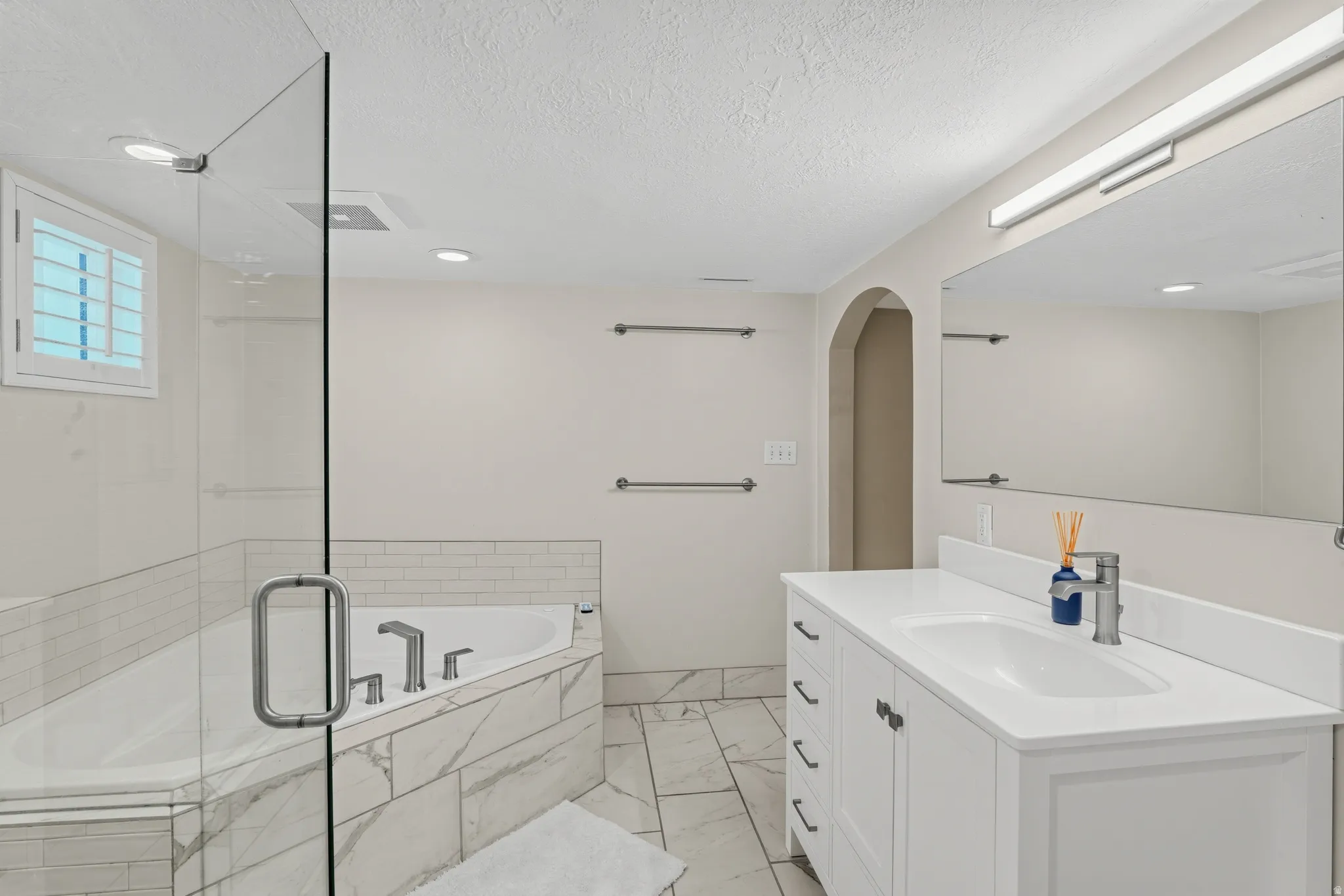 Spacious bathroom featuring a glass-enclosed shower, corner soaking tub, white vanity with integrated sink, and large wall-mounted mirror