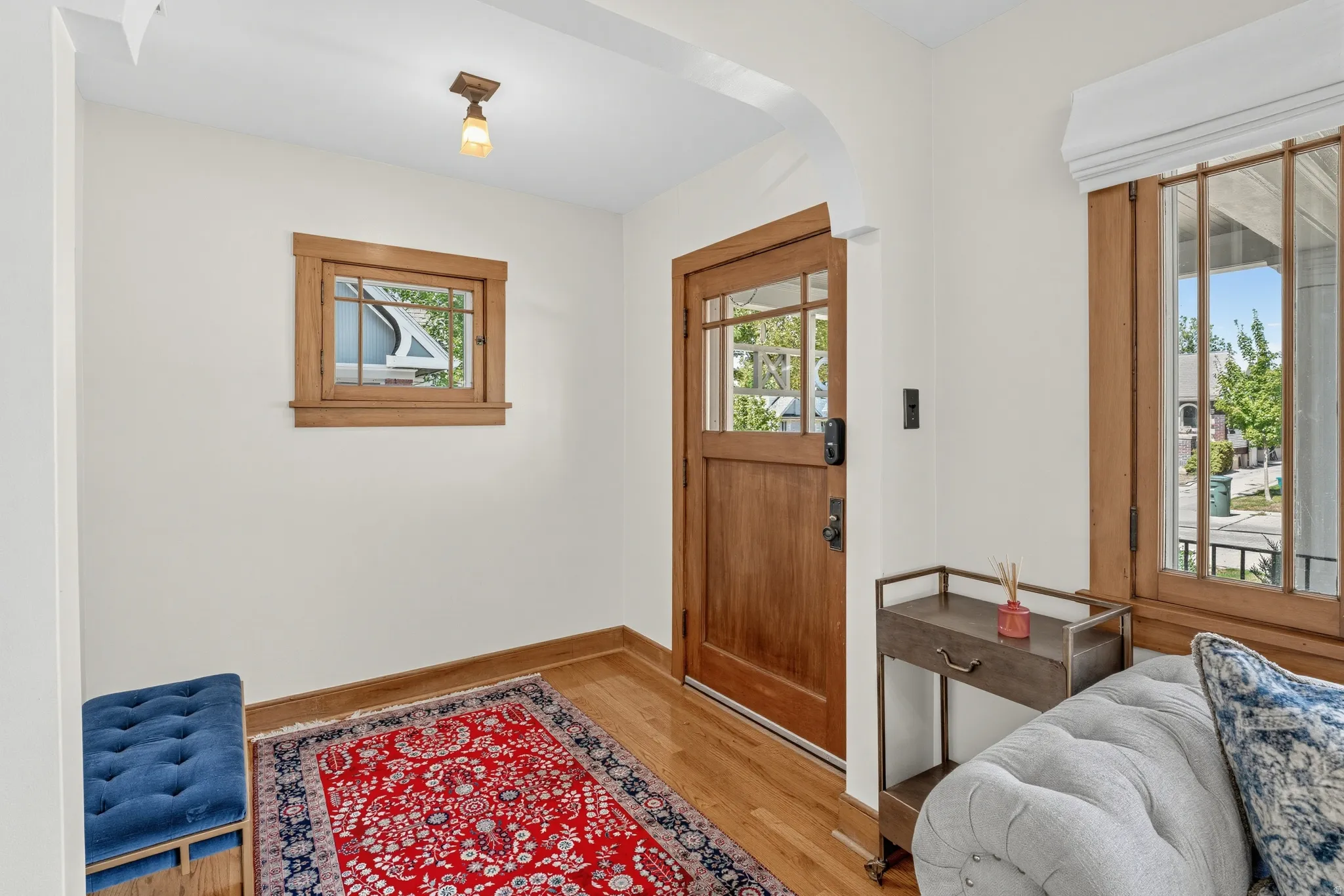 Hardwood flooring, wood-framed windows, wood-paneled door with glass panels, arched entryway, and overhead lighting