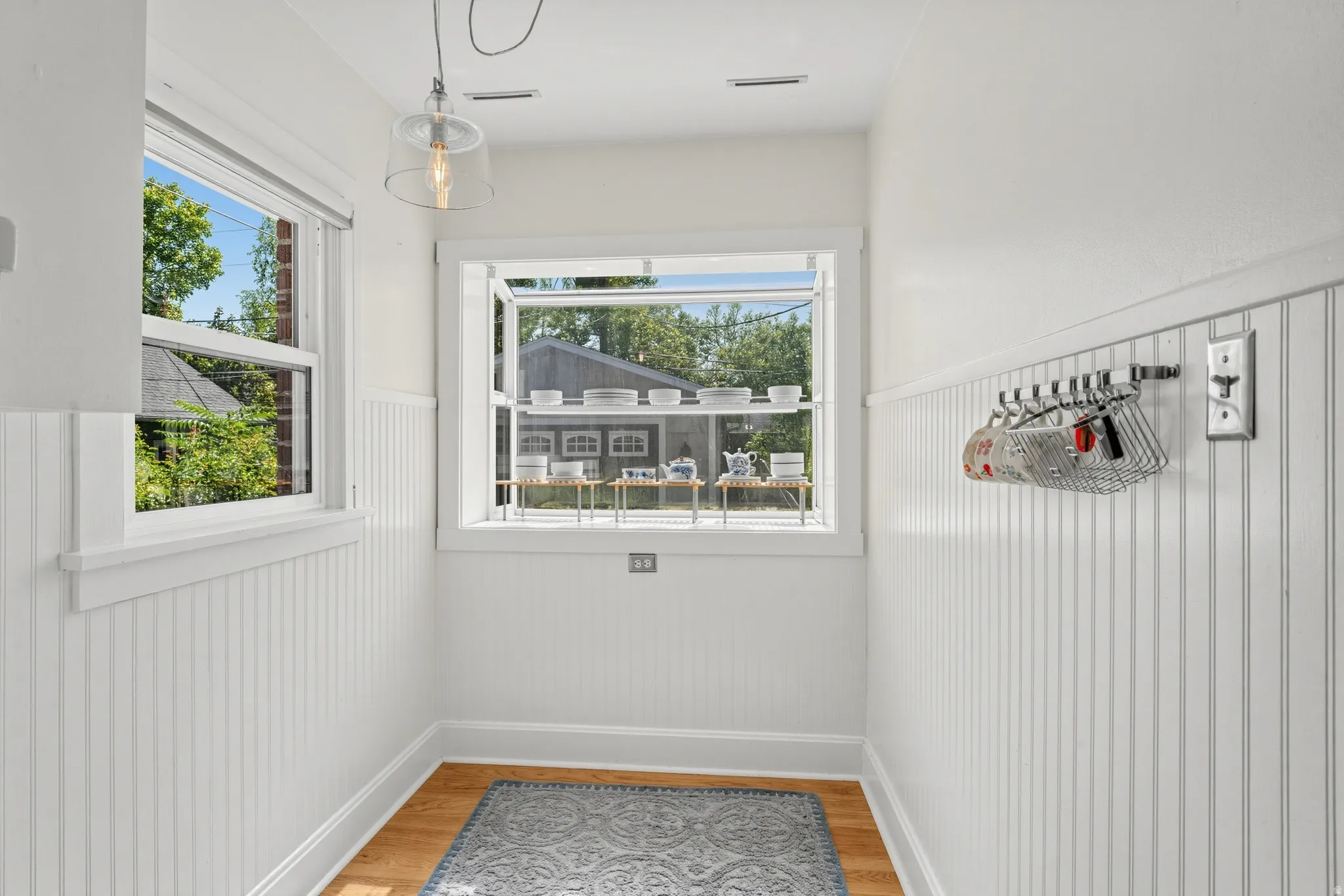 Two windows providing natural light, white beadboard wainscoting, wood-finish flooring, and an overhead pendant light fixture