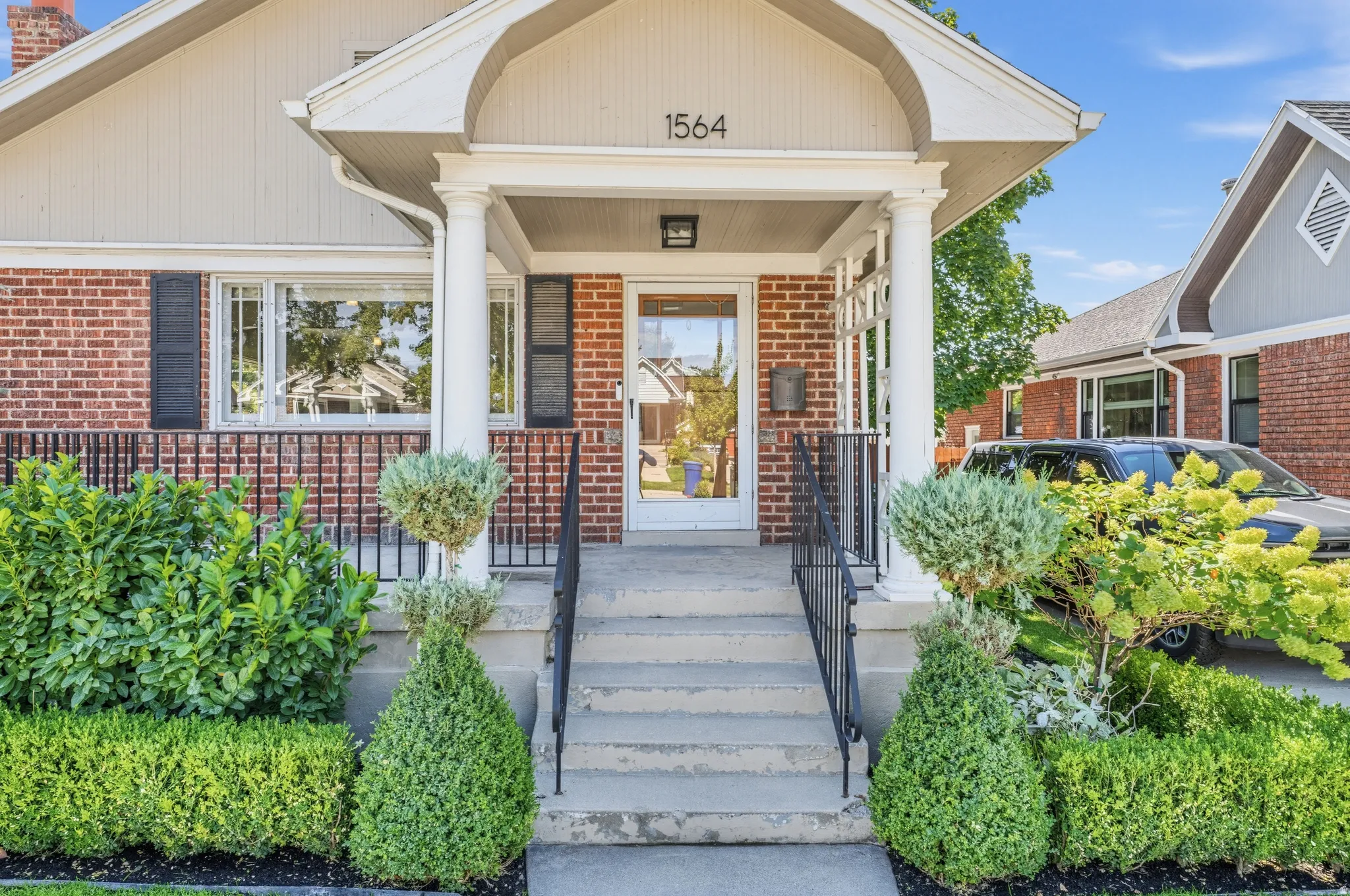 Brick facade with a covered entry, white columns, and black window shutters