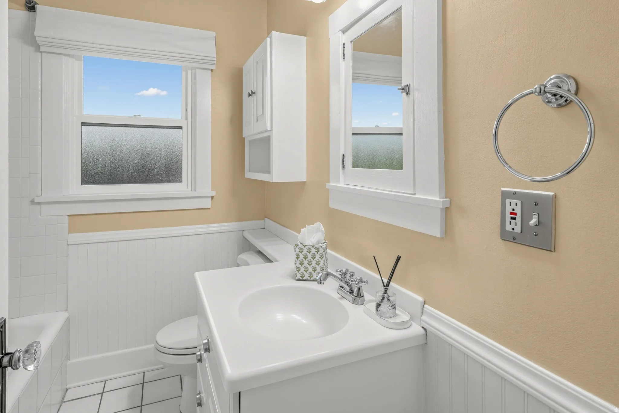 Vanity with integrated sink, chrome faucet, wall-mounted medicine cabinet, white beadboard wainscoting, and white floor tiles