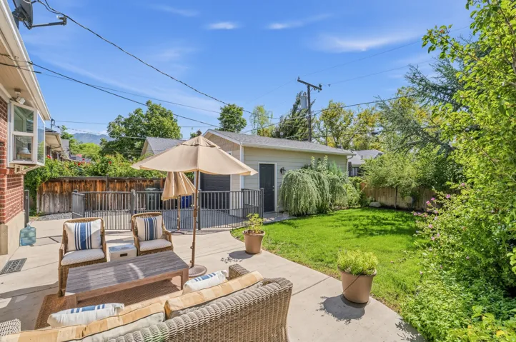 Concrete patio with a brick exterior, bay window, privacy fencing, and a detached structure