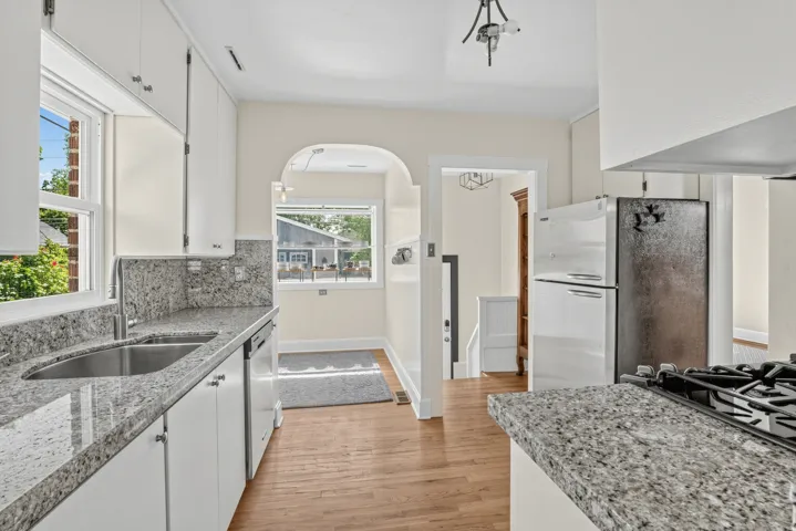 Galley kitchen featuring granite countertops, a stainless steel sink, white cabinetry, and wood-finish flooring