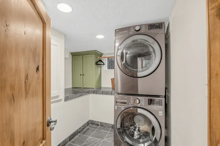 Laundry area featuring stacked appliances, stone-finish flooring, a stone-finish counter, and built-in cabinetry