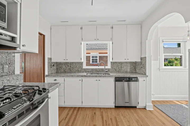 White shaker cabinetry, stone countertops with backsplash, stainless steel appliances, wood-finish flooring, and an arched doorway