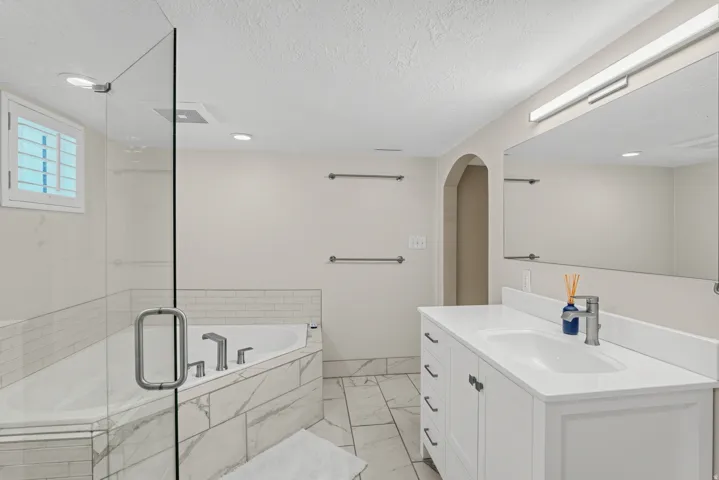 Spacious bathroom featuring a glass-enclosed shower, corner soaking tub, white vanity with integrated sink, and large wall-mounted mirror