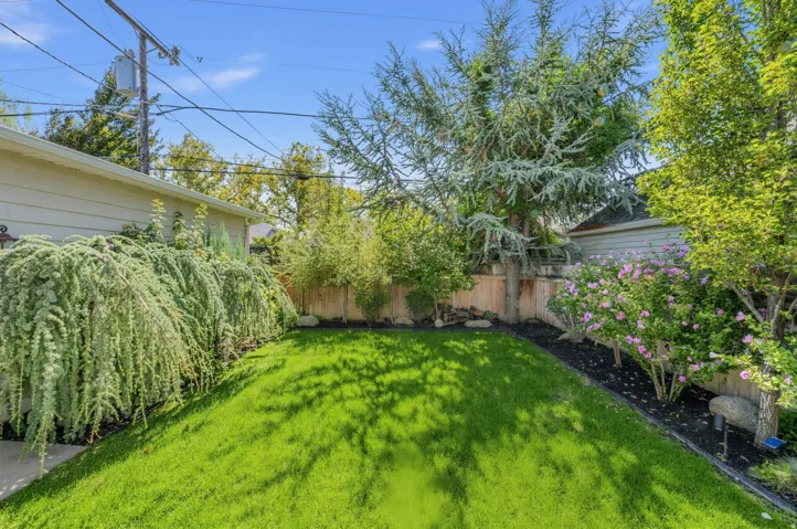 Manicured lawn with a partial wood privacy fence, mature trees, and flowering shrubs