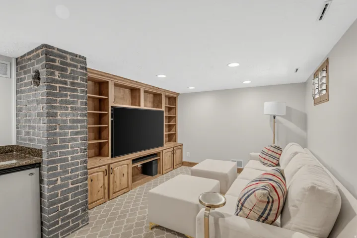 Built-in entertainment center with wood cabinetry and shelving, recessed lighting, brick accent wall, and a built-in wet bar with a compact refrigerator and stone-finish countertop