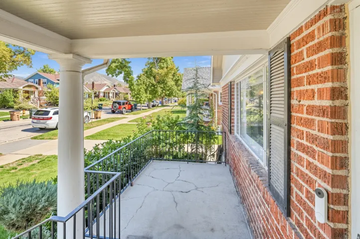 Front porch featuring brick exterior, decorative black shutters, white columns, and wrought iron railings