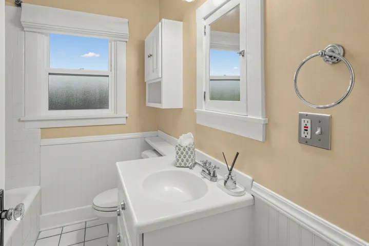Vanity with integrated sink, chrome faucet, wall-mounted medicine cabinet, white beadboard wainscoting, and white floor tiles