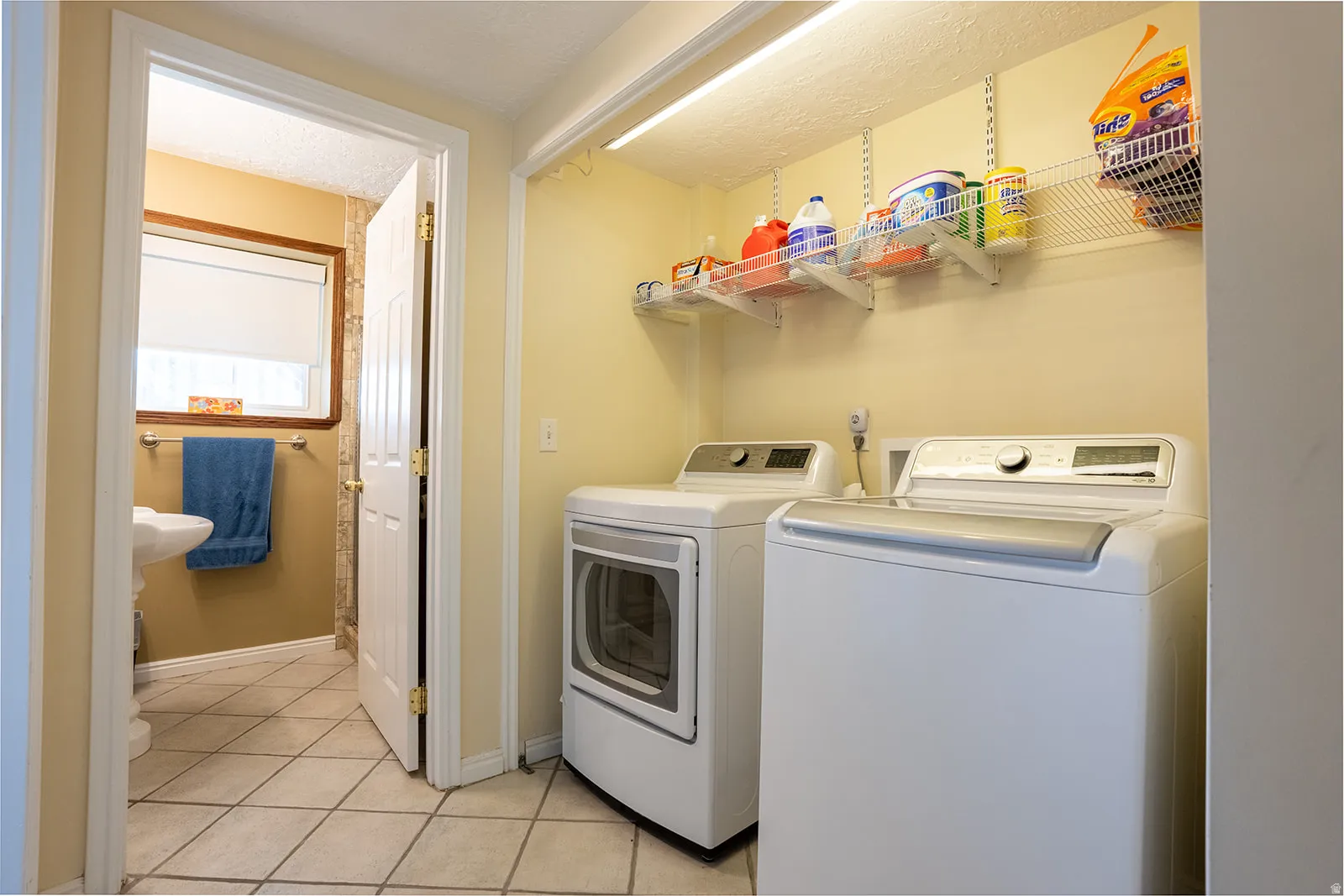 Dedicated laundry area with shelving, overhead lighting, and tiled flooring