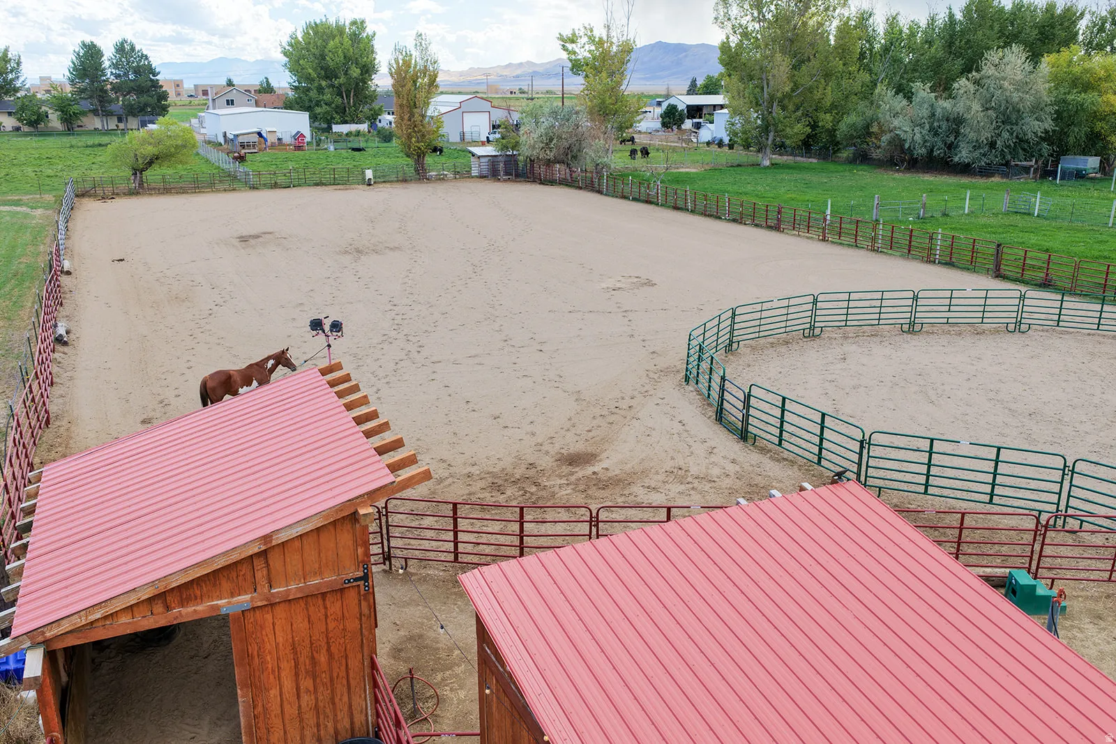 Expansive outdoor arena, round pen with metal fencing, and two wood-sided structures with red metal roofs