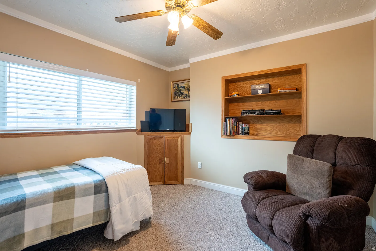 Recessed built-in shelving, wood-finish ceiling fan with lighting, wall-mounted cabinetry, and broad window with blinds