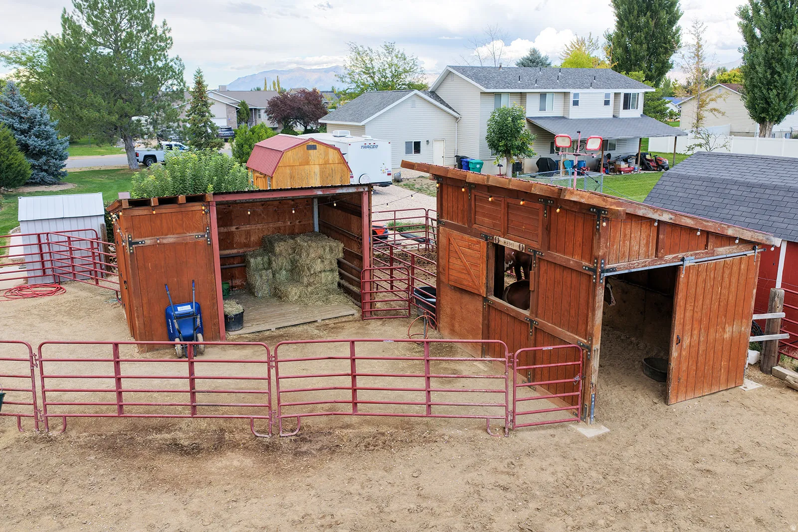 Wood-sided shelters with metal roofing, red metal fencing, and a gravel surface