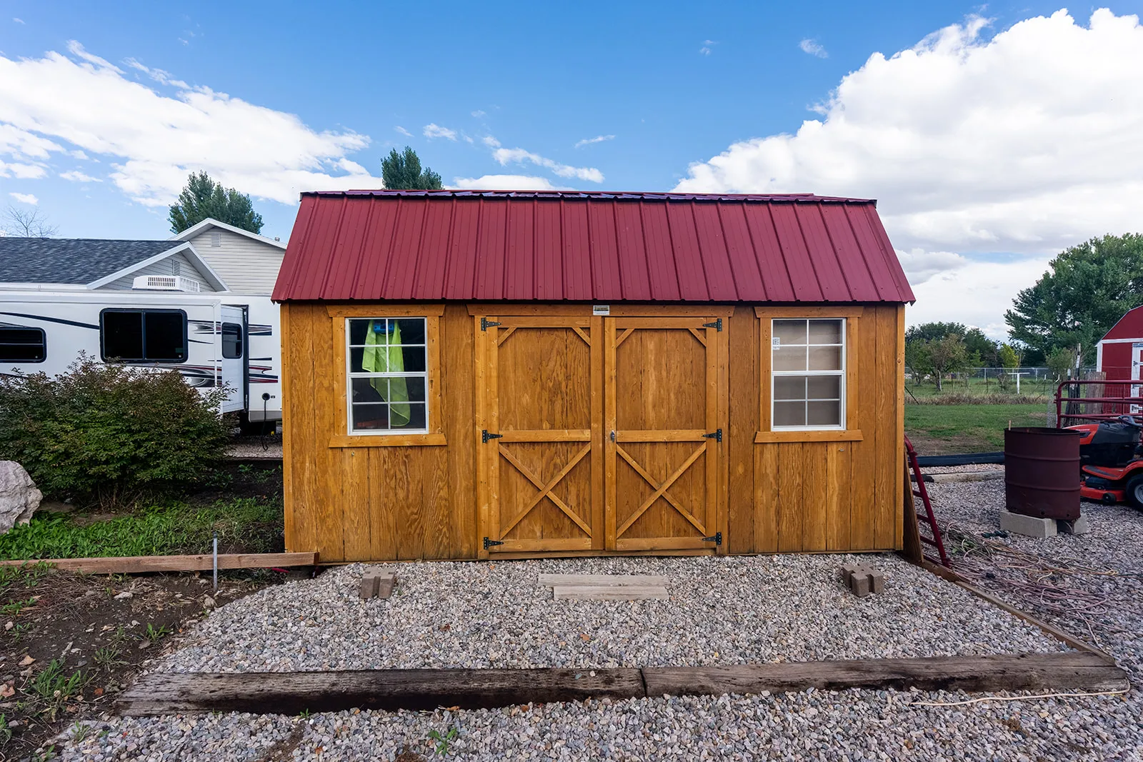 Wood-finish storage shed with a red metal roof and two front-facing windows