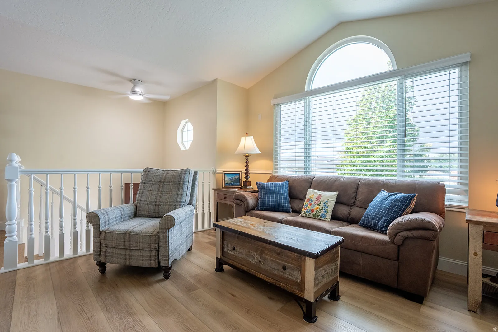Vaulted ceiling, arched transom window, large window with blinds, wood-finish flooring, white railing