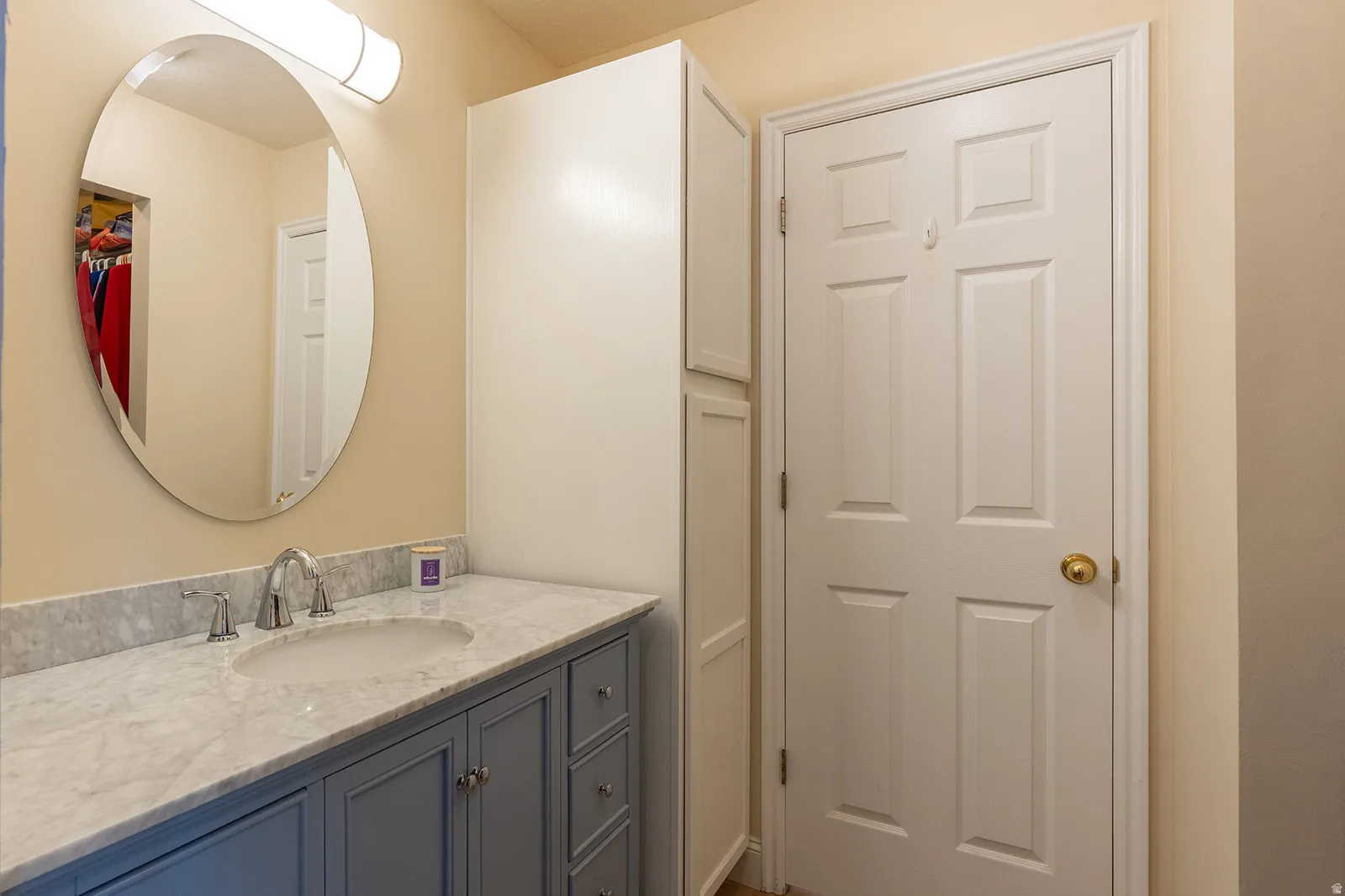 Oval vanity mirror with a chrome faucet, light-toned countertop, and blue-painted vanity cabinetry