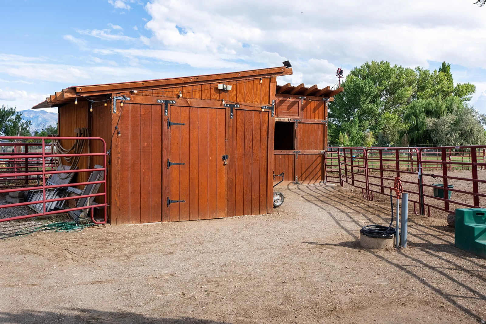 Wood-sided outbuilding with an overhang, featuring multiple gates and fencing