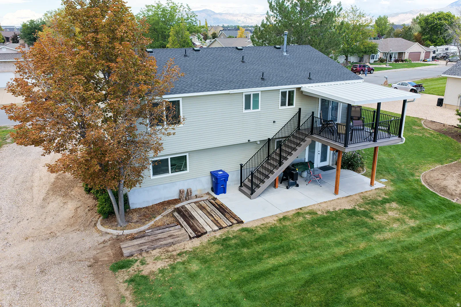 Two-story exterior with light-colored siding, a covered upper deck with black railings, and an exterior staircase descending to a concrete patio